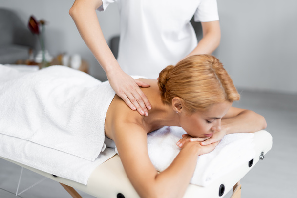 masseur doen schouder massage naar blond cliënt met gesloten ogen  - Foto, afbeelding