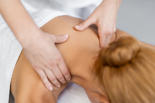 обрезанный вид массажера, делающего массаж плеч белокурой клиентке  - Фото, изображение