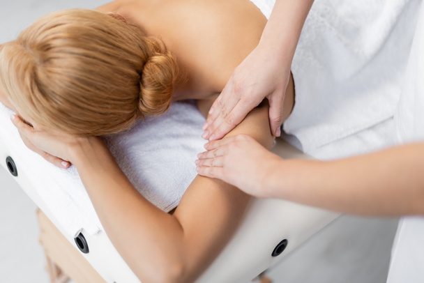 masajista haciendo masaje de hombros a cliente rubio con los ojos cerrados  - Foto, imagen