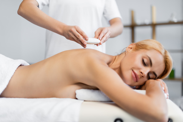 masseur het plaatsen van hot stone op blonde client in spa centrum  - Foto, afbeelding