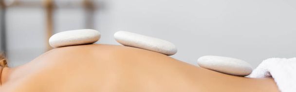 bijgesneden uitzicht op vrouw ontvangen hete steen massage in spa centrum, banner - Foto, afbeelding