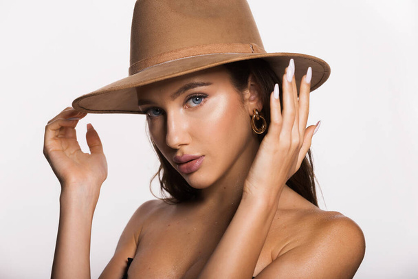 Stylish woman with blue eyes bare shoulder in beige hat covers bare breasts with hands isolated on white background copy space. Sun protection accessories. Travel tour and summer outfit. - Photo, Image