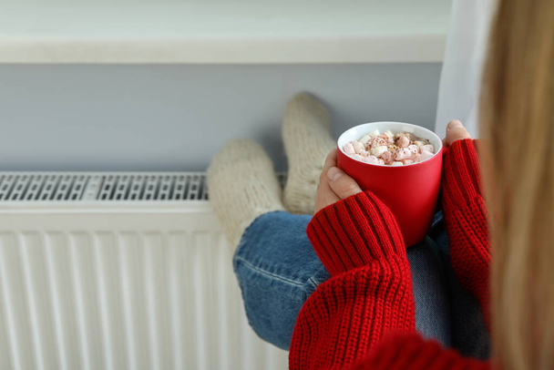Femme avec une tasse de cacao réchauffe ses pieds par le radiateur - Photo, image