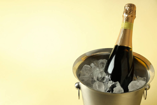 Cubo de metal con hielo y botella de champán sobre fondo beige. - Foto, Imagen