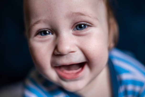 A smiling toothless kid in a striped blouse laughs, face close-up.  - Foto, immagini