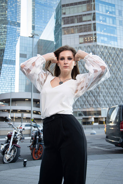 Serious young business woman with modern skyscrapers behind - Фото, изображение
