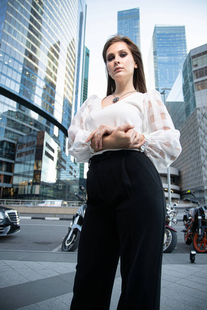 Young business woman with modern skyscrapers behind with folded hands - Foto, Imagen