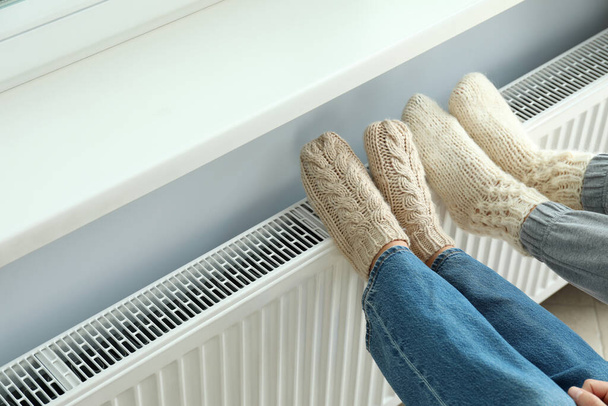 Έννοια της εποχής θέρμανσης με πόδια σε πλεκτές μπότες στο καλοριφέρ. - Φωτογραφία, εικόνα