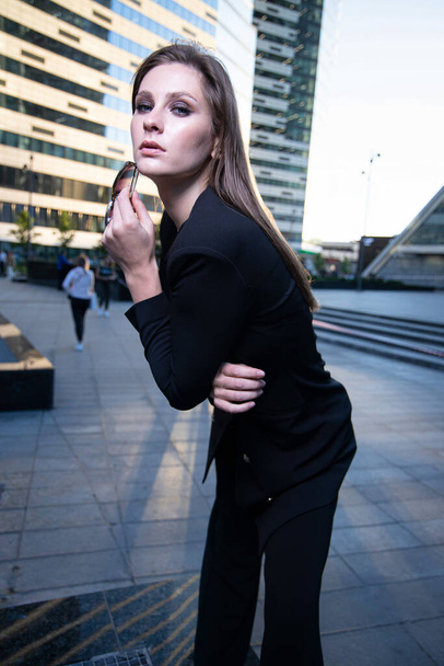 Young business woman on the street of a modern city in black suit - Foto, afbeelding