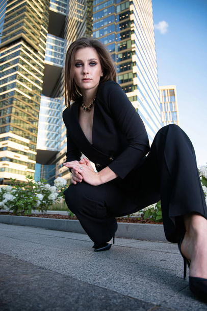 Young business woman in modern city of skyscapers in black - 写真・画像