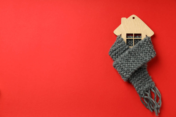 Ξύλινο σπίτι με πλεκτό μαντήλι σε κόκκινο φόντο. - Φωτογραφία, εικόνα