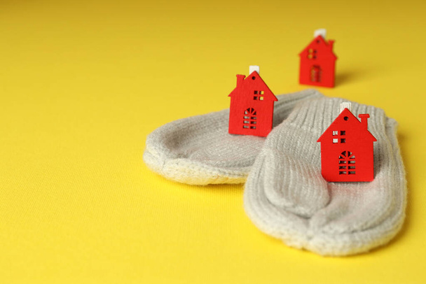 Έννοια της εποχής θέρμανσης με γάντια και κόκκινα σπίτια σε κίτρινο φόντο. - Φωτογραφία, εικόνα