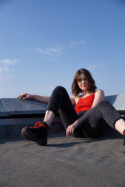 Sitting young white european woman with dark hair on the roof with clear sky behind - Foto, Imagem