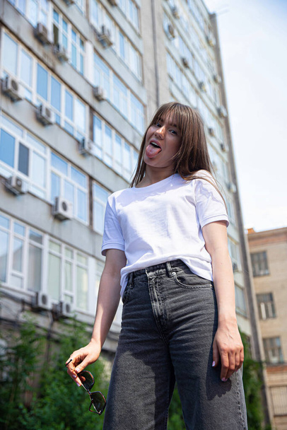 White european young girl with dark hair with building behind with tongue out - Fotó, kép
