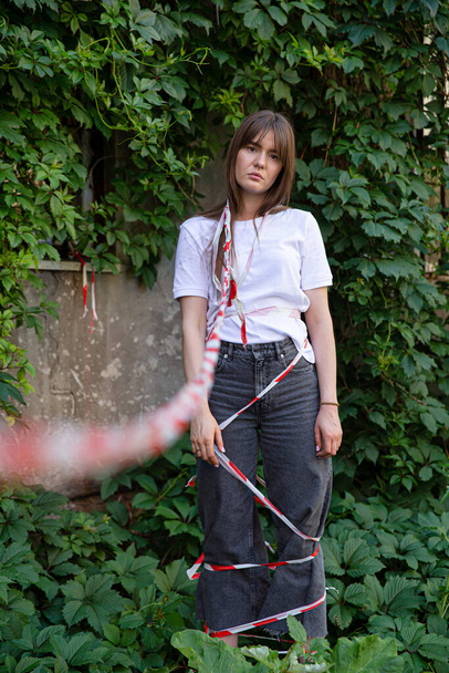 Sad european young girl with dark hair near old wall covered with plants tied up by restrictive tape - Foto, immagini
