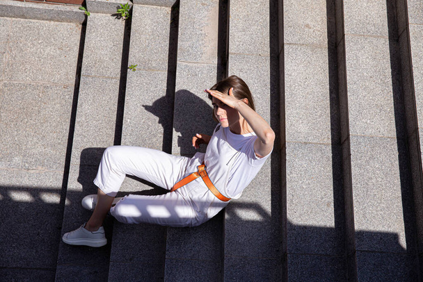 Hiding from the sun young white girl with long hair sitting outside on stairs - Fotoğraf, Görsel