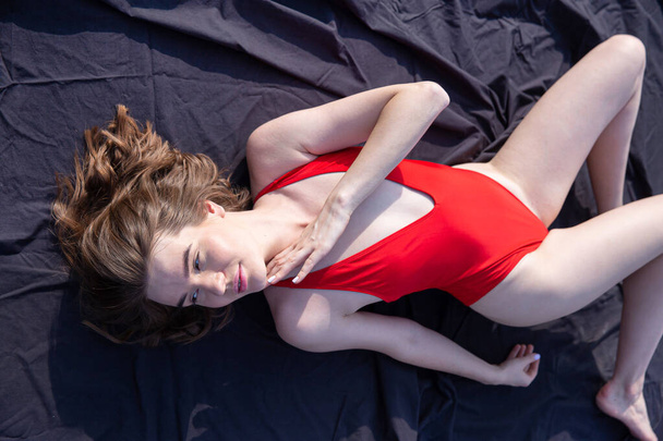 Young caucasian woman in red swimsuit lying on black cloth - Valokuva, kuva