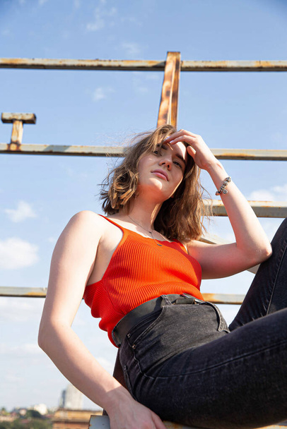 Brown haired young european woman in red top and dark jeans sitting on metal construction - Fotografie, Obrázek