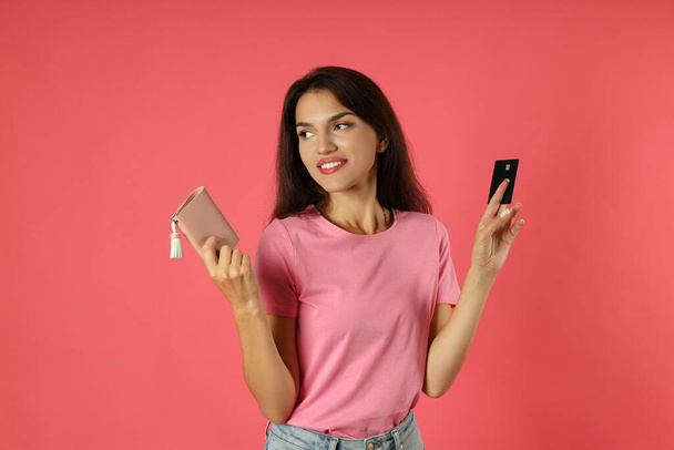 Atraktivní dívka drží kreditní kartu a kabelku na růžovém pozadí. - Fotografie, Obrázek
