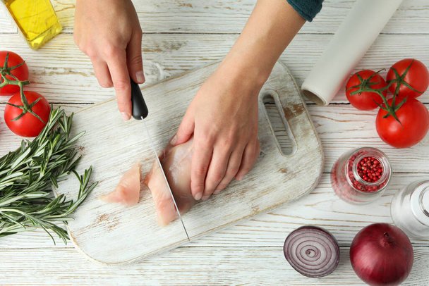 Manos femeninas cortan filete de pollo crudo en tablero de madera - Foto, imagen