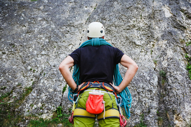Young healthy man wearing in climbing equipment with rope standing in front of a stone rock and preparing to climb - Fotografie, Obrázek