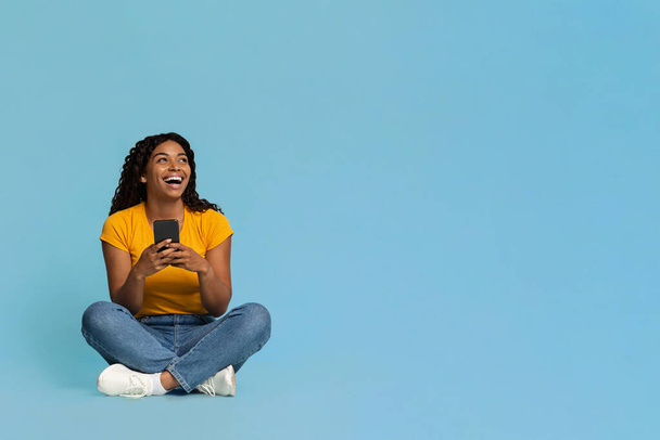 Lachende schwarze Frau mit Handy schaut in Kopierraum - Foto, Bild