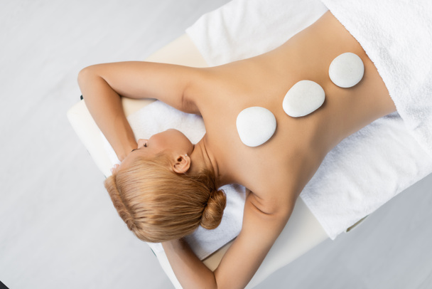 Ansicht von oben: Blonde Frau mit geschlossenen Augen erhält Hot-Stone-Massage im Wellness-Center  - Foto, Bild