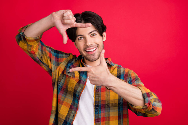 Photo of funky sweet young gentleman wear plaid outfit smiling showing photo shoot gesture isolated red color background - Foto, afbeelding