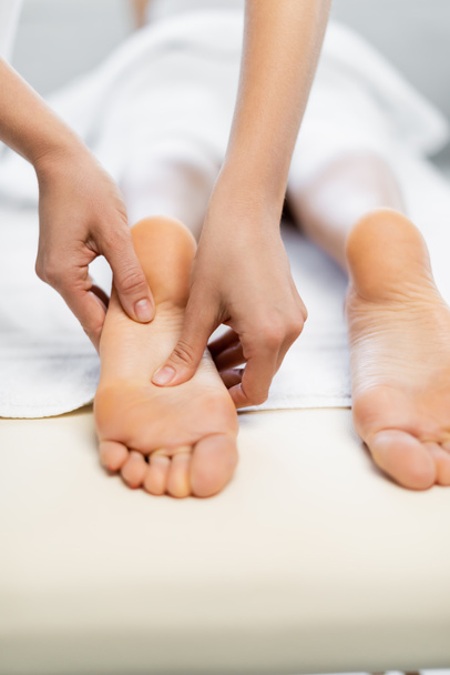 Обрезанный вид массажера, делающего массаж ног женщине на массажном столе
 - Фото, изображение