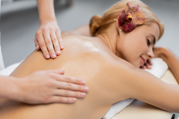 masażysta wcierając olejek do masażu w plecy rozmytego klienta - Zdjęcie, obraz