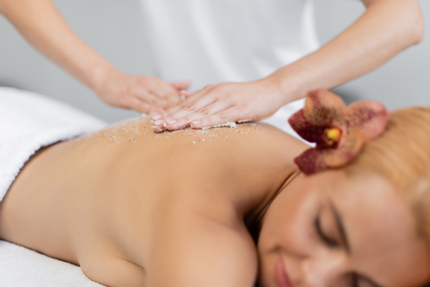 professionele masseur aanbrengen lichaam scrub op de rug van wazig cliënt  - Foto, afbeelding