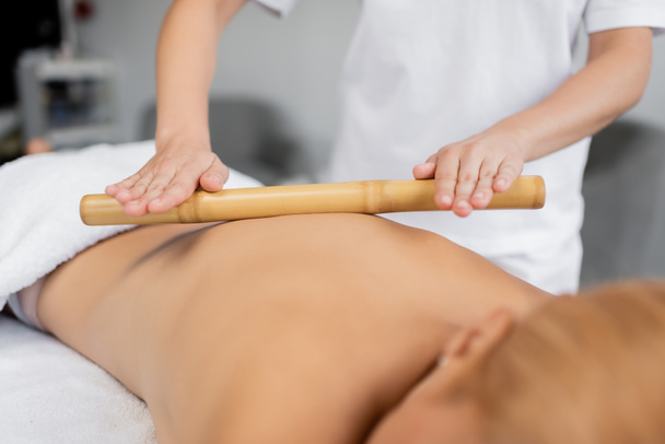 vista parziale del massaggiatore professionista massaggiando schiena del cliente con bastone di bambù - Foto, immagini