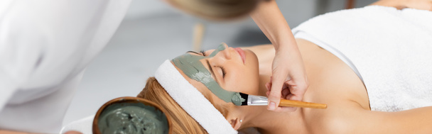 esteticista segurando tigela e aplicando máscara de barro no rosto da mulher no centro de spa, banner - Foto, Imagem