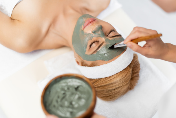 косметолог наносить глиняну маску на блондинку, лежачи на масажному столі
 - Фото, зображення