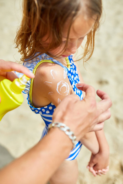 Papa cremt seine Tochter am Strand ein, Vater streicht sich Sonnencreme über die Schulter in Form der Sonne, schützt die Haut mit Sonnencreme. Sommerferien. - Foto, Bild