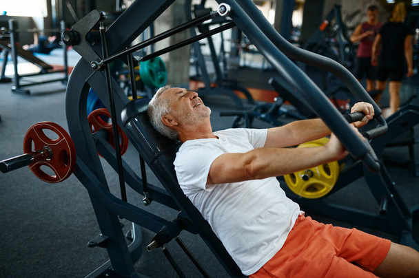 Cheerful old man on exercise machine in gym - 写真・画像