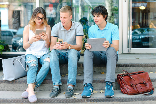 Jeunes trois amis assis par terre dans la rue, parlant, utilisant
 - Photo, image