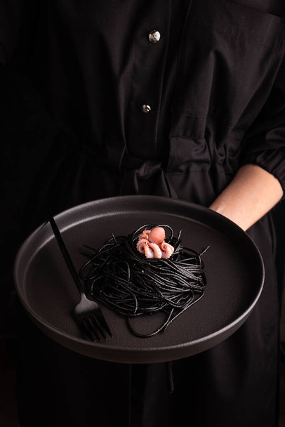 Woman holding a plate with black spaghetti with boiled octopus - Φωτογραφία, εικόνα