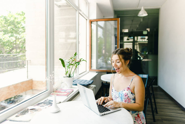 Fiatal boldog lány ül a kávézóban, és szörfözés internet laptoppal. - Fotó, kép