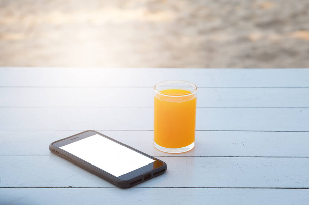 Orange juice in glass and mobile phone on white wooden table background - Photo, Image