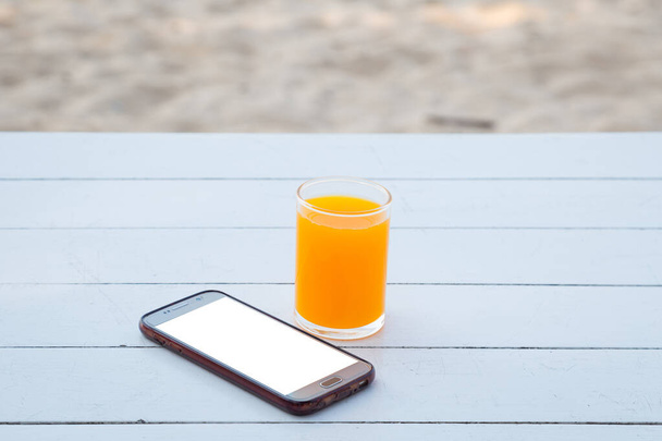 Pomerančová šťáva ve skle a mobilním telefonu na bílém dřevěném stole pozadí - Fotografie, Obrázek