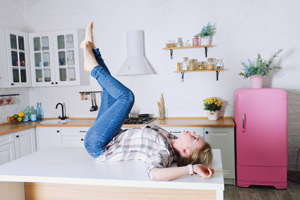 Giovane donna bionda carina 30 + in blue jeans e una camicia seduta e rilassante nella sua luminosa cucina pulita. Stile di vita sano e felice. Tempo libero. - Foto, immagini