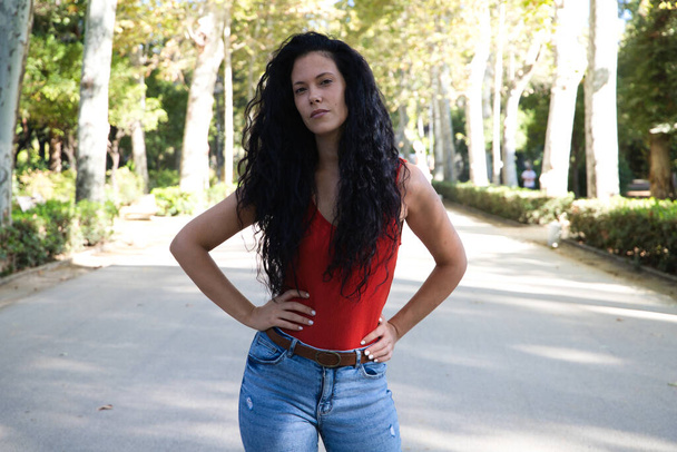beautiful adult woman, brunette with curly hair and gypsy latin features is on a road and on the sides giant trees, the woman is making different gestures and poses. Concept expressions - Photo, Image