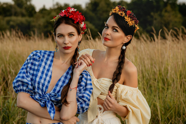 Young girls dressed in white and blue dress pose against the background of nature, and hold a basket of flowers in their hands. - Foto, imagen