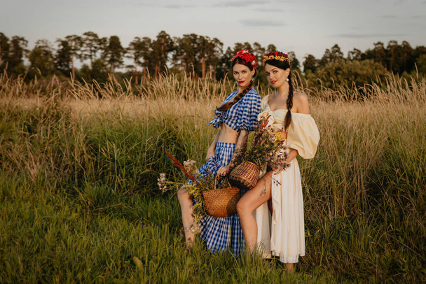 自然を背景に白と青のドレス姿の少女たちがポーズをとり、花の籠を手にしている。. - 写真・画像