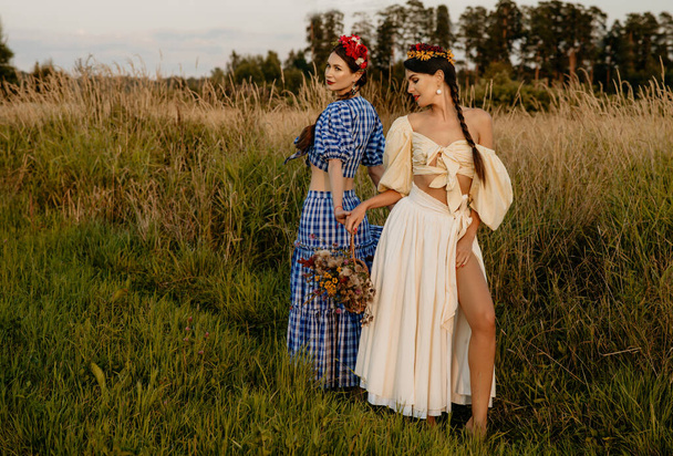 Young girls dressed in white and blue dress pose against the background of nature, and hold a basket of flowers in their hands. - Φωτογραφία, εικόνα