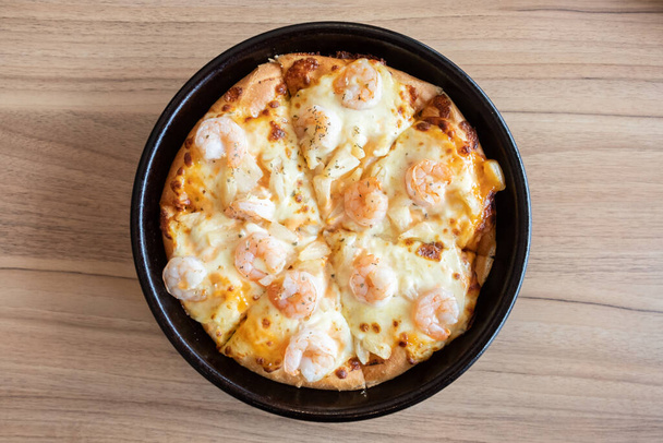 Close up of delicious seafood pizza topped with cheese, pineapple and shrimp on wooden table. Pizza is a favorite food for many around the world. - Photo, Image