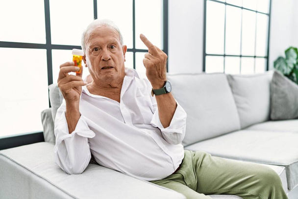 Senior man holding pills showing middle finger, impolite and rude fuck off expression  - Foto, Bild