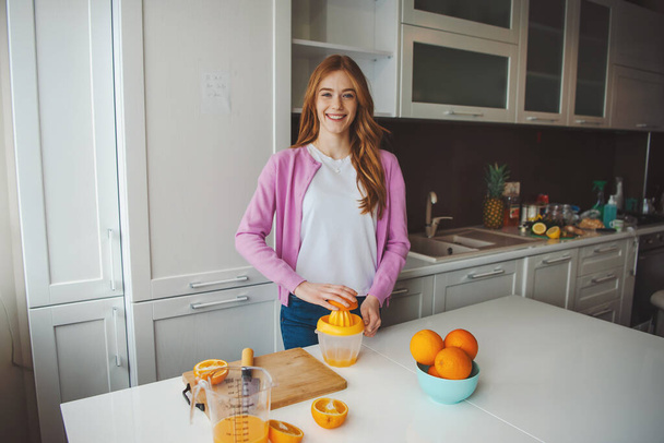 Kobieta ciesząca się porankiem w kuchni robi sok pomarańczowy. Zdrowa dieta - Zdjęcie, obraz