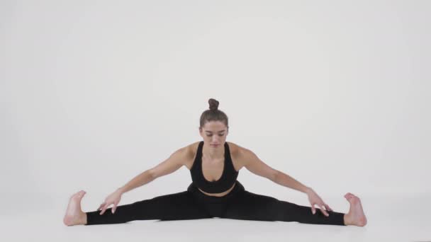 Nuori, joustava nainen istuu lattialla jalat levällään ja nojaa eteenpäin, harjoitellen Upavistha Konasanan asentoa - Materiaali, video